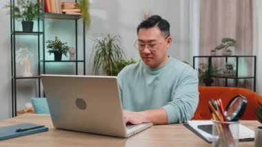 Asyalı adam evdeki masadaki oturma odasında işini bitirdikten sonra bilgisayarı kapatıyor. Çevrimiçi çalışan serbest çalışan bir adam, uzaktan kumanda. Defter bilgisayarında e-öğrenme, internette gezinme