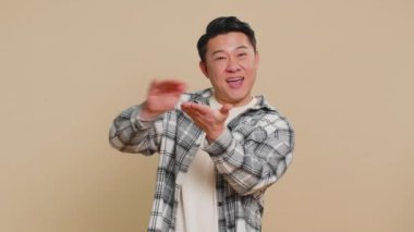 Tişörtlü mutlu Asyalı adam daha fazla bahşiş dağıtırken daha fazla bahşiş dağıtırken, büyük ikramiye kazanırken, başarılı bir alışveriş ödemesi yaparken para kaybediyor. Bej arka plandaki Çinli adam.