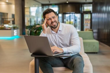 Baş ağrısı, tansiyon, migren ve modern ofis lobisindeki stresten muzdarip yorgun ve genç bir işadamı. Otel koridorunda dizüstü bilgisayar ağı üzerinde çalışan yakışıklı, serbest çalışan bir adam. Fazla çalışma