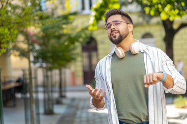 Ciddi derecede tatminsiz, gözlüklü, dışarıda duran, sinirli bakışları olan, geç kaldığı için üzülen, kol saatine dokunan, sinirli birini arayan, beyaz bir turist.