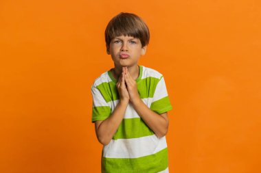 Lütfen, Tanrım yardım et. Ergen çocuk dua ediyor, dilek diliyor, umutlu bir şekilde yalvarıyor, özür diliyor, kötü davranışları için onu cezalandırmamayı diliyor. Turuncu arka planda küçük çocuklar