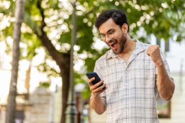 Cep telefonu kutlaması yapan Hintli genç adam iyi haber kazandı, piyango büyük ikramiyesi kazandı, açık havada dağıttı. Şehir sokağındaki İspanyol adam. Kasaba yaşam tarzları. Yatay.