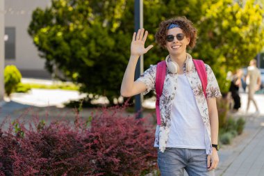 Neşeli genç turist, kameraya gülümseyen, el sallayan, el sallayan davetkar merhaba, merhaba, merhaba, güle güle, misafirperver bir yüz ifadesiyle hoş geldiniz. Şehir merkezindeki adam..