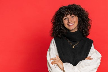 Kıvırcık saçlı, mutlu beyaz kadın portresi. Dostça gülümseyen, kameraya bakan mutlu yüz ifadesi. Hayal kuruyor, dinleniyor, rahatlıyor. İçerideki kız kırmızı arka planda