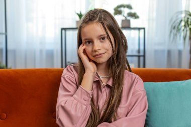 Mutlu gülümseyen genç kız çocuğunun portresi rahat koltukta oturup evdeki oturma odasındaki kameraya bakıyor. Kahverengi uzun saçlı, tatlı, genç bir kız öğrenci. Yaşam Tarzları.