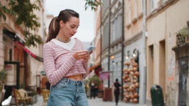 Gezgin genç bir kadın akıllı telefon kullanıyor cep telefonu navigatör uygulamasında haritada arama yapmak için kısa mesajlar yazıyor. Beyaz kız şehir sokağından geçiyor.