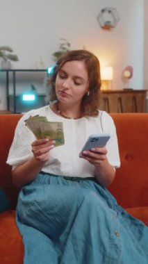 Başarılı zengin kadın akıllı telefon tutuyor ve evdeki kanepede oturan Avro Faturası hayranını sallıyor. Mutlu kız çevrimiçi piyango oyunu kazandı. Tatil planlama, bütçe hesaplama. Dikey