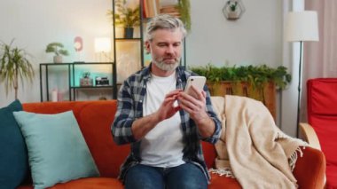 Evdeki koltukta oturan mutlu, olgun bir adam akıllı telefon kullanan eski bir dostundan mesaj alıyor. Gülümseyerek yüzünü yana çevir. Beyaz saçlı, yaşlı bir adam evdeki oturma odasında telefon ekranından iyi haberler okuyor.