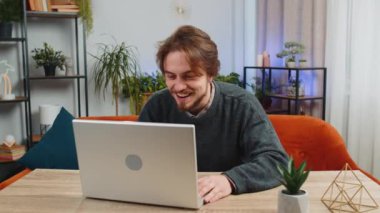 Laptop bilgisayar kullanan beyaz bir adam, iyi haber mesajı alıyor. Aniden kazanılan piyango galibiyetini kutluyor. Evdeki dairede online alışveriş oyunu oynanıyor.