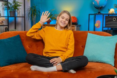 Beyaz çocuk evde mutlu bir şekilde selamlaşırken gülümseyerek el sallıyor. Kanepeye oturur, kameraya bakar, neşeyle merhaba der hoş geldin der ya da elveda der, neşe ve dostluk sergiler.