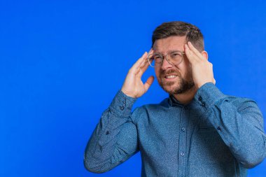 Baş ağrısını tedavi etmek için tapınak ovalayan gözlüklü, yorgun, orta yaşlı bir adam gergin migren stresinden muzdarip. Acı içinde kıvranan genç bir adam mavi arka planda yüksek tansiyon.
