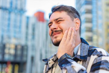 Şehir merkezindeki caddede dikilen olgun beyaz erkek diş ağrısı, kötü semptomlar, yanak çenesinde el tutmaktan muzdarip adam diş sinirlerine zarar veren tıbbi yardıma ihtiyacı var..