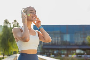 Sporcu spor koşucusu kız eğitiminin yan görüntüsü, kablosuz kulaklık takmak ve favori müzik dinlemek. Şehir parkında egzersiz kardiyosu. Genç bir kadın sağlıklı yaşam tarzı için koşuyor..
