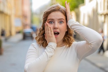 Aman Tanrım, vay canına. Şaşırmış kızıl saçlı kadın kameraya şaşkın şaşkın bakıyor. Büyük, açık gözlerle. Aniden kazanılan galibiyet oyunu galibiyetinin şokuyla dışarıda iyi haberler var. Şehir caddesinde yürüyen kız