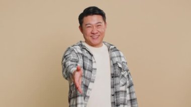 Dost canlısı Asyalı orta yaşlı Çinli adam kameraya uzanmış, el sıkışma teklif ediyor, nazik bir gülümsemeyle selamlıyor, davet ediyor, dayanışma gösteriyor, güven kavramı bej arka planda izole ediliyor.