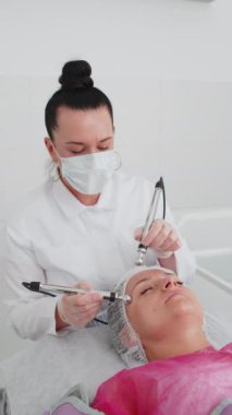 Güzellik uzmanı kadınlara mikro akım yaptırıyor. Spa kliniğinde anti-yaş kız cilt bakımı. Kozmetik doktoru, yüz kozmetik güzellik tedavisi için elektriksel impulslar kullanıyor. Dikey görünüm
