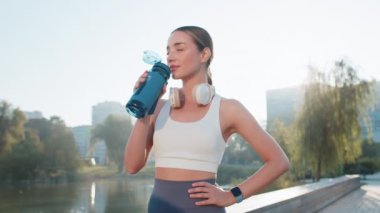 Sporcu formda koşucu kız antrenmandan sonra biberondan su içiyor. Sabah parkta kardiyo çalışacaksın. Genç zayıf kadın koşucu sağlıklı yaşam tarzının tadını çıkarıyor. Aktif sporcu kadın aktiviteleri.