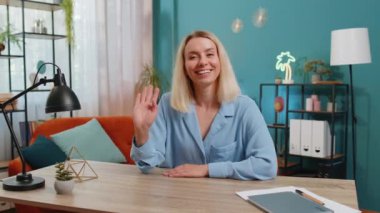 Genç iş kadını kameraya dostça gülümsüyor ve el sallıyor merhaba, merhaba, merhaba ya da güle güle diyerek, ofis çalışma masasında misafirperver bir ifadeyle karşılıyor. Oturma odasında mutlu bir kız.