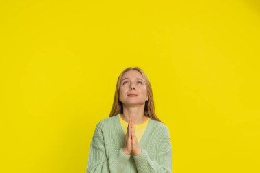 Lütfen, Tanrım yardım et. Kafkasyalı orta yaşlı bir kadın dua ediyor, yukarı bakıyor ve dilek tutuyor, umut dolu bir ifadeyle soruyor, özür diliyor, meditasyon yapıyor. Sarı arka planda izole edilmiş yetişkin bir kız.