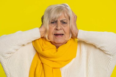 Duymak ve dinlemek istemiyorum. Sinirli, sinirli, yaşlı bir kadın kulaklarını kapatıyor. Tavsiye vermekten kaçınmıyor, gürültülü sesleri görmezden geliyor. Sarı arka planda olgun bir büyükanne.