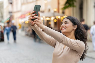 Hintli genç blog yazarı akıllı telefondan selfie çekiyor, abonelerle çevrimiçi video görüşmesi yapıyor, sosyal medya vlog 'u için hikayeler kaydediyor. Şehir caddesinde yürüyen İspanyol kız