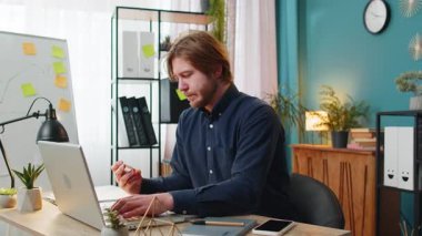 Kafkasyalı mutlu işadamı banka kartı ve dizüstü bilgisayarını merkez ofisteki online alışveriş ödemeleri için kullanıyor. İş anlaşması. Gülümseyen adam netbook E-bankacılık uygulama hizmeti ile serbest alım yapıyor.