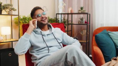 Telefon, iyi haber, dedikodu. Mutlu Hintli adam akıllı telefondan hoş sohbetler ediyor, modern ev odasındaki arkadaşlarıyla konuşmaktan keyif alıyor. Cep telefonundan hoşlanan adam konuşuyor
