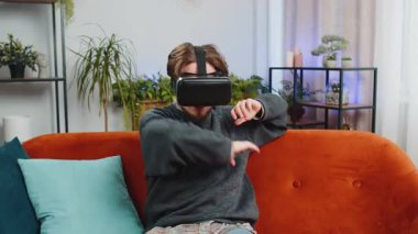 Sakallı adam sanal gerçeklik teknolojisi VR uygulama kulaklığı kullanarak 3D 360 çevrimiçi video oyunu simülasyonu yapıyor ve modern ev dairesinde film izliyor. Gözlüklü adam kanepede oturuyor.