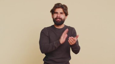 İyi iş çıkardın. Lübnanlı genç adam başparmağını sallıyor ve onaylıyor, el çırpıyor, başarılı bir iş çıkarıyor, tatmin oluyor, kutluyor. Hintli İspanyol adam bej renkli stüdyoda izole edilmiş..