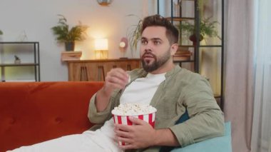 Kafkasyalı rahat genç adam patlamış mısır yiyor ve evdeki oturma odasında kanepede oturup film izliyor. Kahverengi saçlı, sıradan elbiseli mutlu bir adam. Hafta sonu dairede gerilim filmlerinin tadını çıkarıyor..