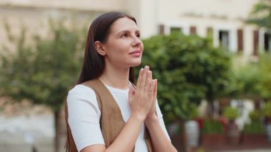 Genç Avrupalı bir kadın Tanrı 'ya kapalı gözlerle dua ediyor dışarıda kutsama, yardım ve af diliyor. Güneşli şehir caddesinde el ele tutuşan güzel kız şans diliyor. Kasaba dini yaşam tarzları.