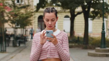 Akıllı telefon kullanarak gülümseyen genç bir kadın. Kısa mesajlar yazarak interneti tarıyor, işi bitiriyor, dışarıdaki kameralara bakıyor. Şehir caddesinde duran kız turist. Kasaba yaşam tarzları.