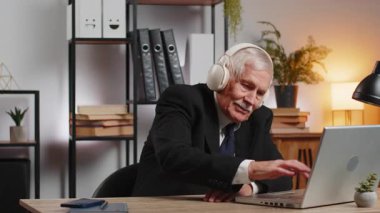 Memnuniyetle ofis masasında oturmuş, kablosuz kulaklıkla en sevilen enerjik müziği dinleyen iş adamı. Heyecanlı serbest çalışan büyükbaba rahatlıyor, masadaki dizüstü bilgisayarla mola veriyor..