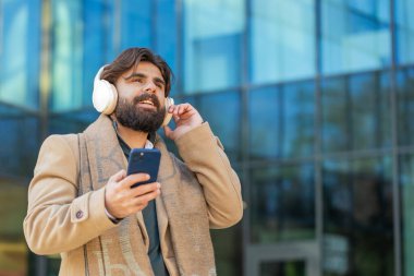 Mutlu Arap işadamı kablosuz kulaklık takıyor, açık havada akıllı telefondan en sevilen enerjik müziği dinliyor. Gülümseyen adam şehir sokağının yanından geçiyor. Yaşam Tarzları.