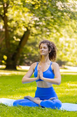 Lotus pozisyonunda oturan genç bir kadın yaz günü parkta dinleniyor. Sportif kaygısız yetişkin kız yoga meditasyonu yapıyor, pozitif enerji alıyor, sağlıklı yaşam tarzı. Aktif sporcu kadın.