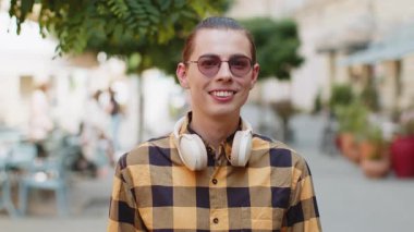Boynuna kulaklık takmış mutlu bir adamın portresi dostça gülümsüyor, kameraya bakıp hayal kuruyor, dinleniyor, rahatlıyor dışarıda iyi haberler veriyor. Şehir sokağındaki genç adam..