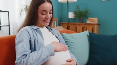 Evdeki rahat koltukta oturan, göbeğini okşayan, rüya gören, mutlu, hamile bir kadın. Hamilelik sırasında gülümseyen, beyaz, müstakbel kadın anne bebek bekliyor..