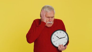 Endişeli yaşlı bir adam, saati kontrol ediyor, işe geç kalıyor, gecikiyor, son teslim tarihi. Yaşlı büyükbaba saat, dakika bakıyor, sarı arka planda dakikası dakikasına izole edilmekten endişe ediyor.