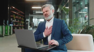 Diz üstü bilgisayar kullanan ve modern ofis lobisinde çalışırken kalp krizi geçirme riski taşıyan gerilimden muzdarip Kafkasyalı yetişkin işadamı. Takım elbiseli iş adamı.