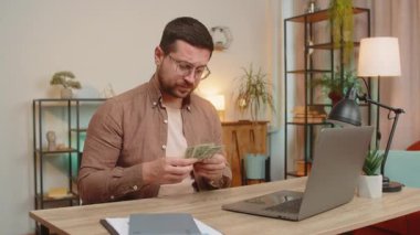 Kafkasyalı serbest çalışan bir adam dolar sayıyor. Yetersiz miktarda para. Finansal kriz. İflas. Yoksulluk ve yoksulluk. Ev ofis masasında dizüstü bilgisayarı olan üzgün bir iş adamı oturuyor..