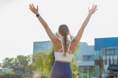 Güneşli bir günde şehir parkında koşu yaptıktan sonra başarıyı kutlayan heyecanlı beyaz atletik kadın koşucusunun arka görüntüsü. Koşu şampiyonu maratonu kazanıyor. Aktif sporcu kadın motivasyonu.