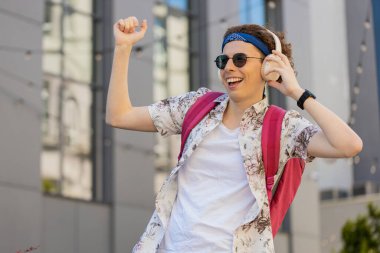 Kablosuz kulaklıklı, dans eden, açık havada en sevilen enerjik disko müziğini dinleyen mutlu, rahat, beyaz bir adam. Kıvırcık saçlı ve sırt çantalı neşeli turist şehirde yürüyor..