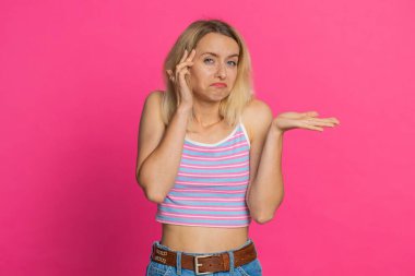 Ne diyecegimi bilmiyorum. Kafası karışmış Kafkasyalı genç bir kadın belirsiz bir sorudan utanıyor, şüpheleri var, cevap yok, fikir yok, kararsız. Sarışın kız pembe arka planda izole edilmiş.