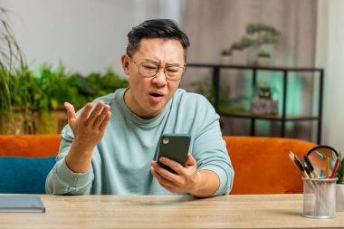 Hüzünlü Çinli adam akıllı telefon daktilo kullanıyor, beklenmedik piyango sonuçlarını kaybediyor, kötü haber, servet kaybı, son teslim tarihi, virüs. Olgun Asyalı çocuk kanepede oturuyor.