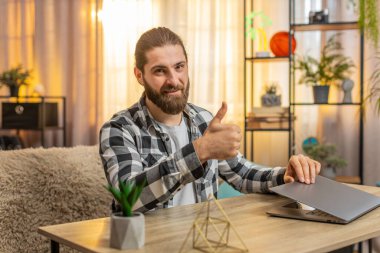 Mutlu gülümseyen genç adam ev masasındaki görevlerini tamamlıyor, bilgisayarını minnettar bir ifadeyle kapatıyor. Kanepede oturan beyaz bir adam kameraya doğru dönüyor, iyi bir iş çıkardığını söylüyor..