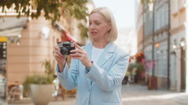Gülümseyen mutlu, heyecanlı, Kafkasyalı, resmi takım elbiseli iş kadını fotoğrafçı. Büyüleyici şehrin fotoğraflarını çekmek için klasik kamera kullanıyor. Seyahat, hobi konsepti. Şehir sokağındaki bayan işveren..