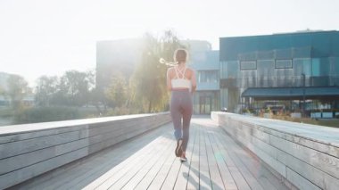 Antrenman maratonunda koşan, kulaklıkla müzik dinleyen aktif sporcu kadının arka görüntüsü. Şehir parkında kardiyo çalışması. Genç kız sağlıklı yaşam tarzını seviyor. Kadın atlet koşucu.