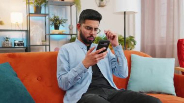 Akıllı telefon kullanan üzgün Hintli genç adam olumsuz mesaj okurken oturma odasındaki kanepede oturmaktan rahatsız oluyor. Eli başının üstünde olan İspanyol adamın evinde alet sorunu var. Uygulama çökme konsepti.