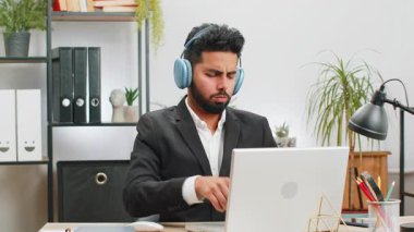 Mutlu, aşırı mutlu Hintli iş adamı ev bilgisayarında çalışıyor kulaklık takıyor ve en sevilen enerjik disko müziğini dinliyor ve dans ediyor. Serbest çalışan adam dinleniyor, mola veriyor.