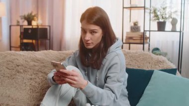 Hoşlanmamak. Kafkasyalı kadın akıllı telefonu evdeki kanepede otururken kullanıyor. İşaret işareti işareti yapıyor, hoşnutsuzluğunu dile getiriyor, tatminsiz kötü işleri tasvip ediyor. Memnun olmayan kız başını sallar..